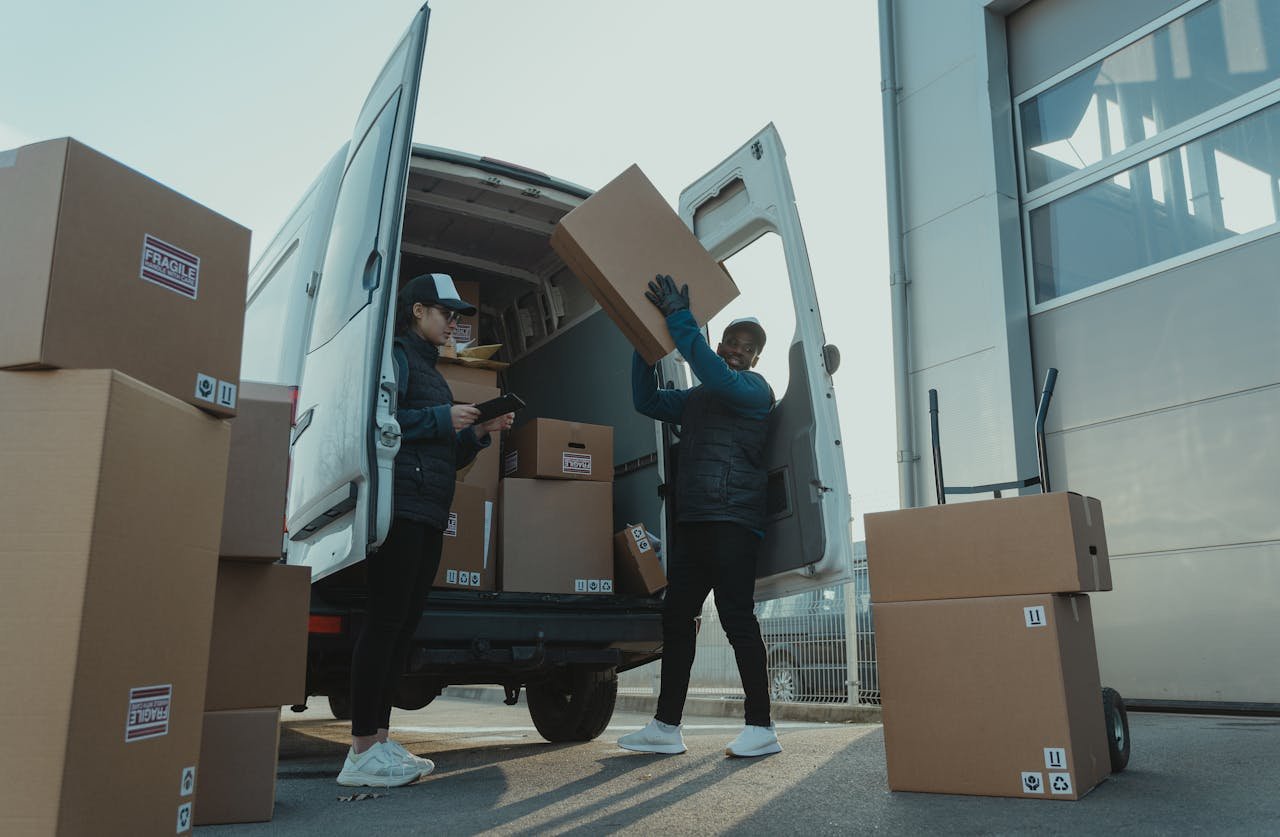 hero-img-01 Workers loading boxes into a delivery van at a warehouse facility outdoors.