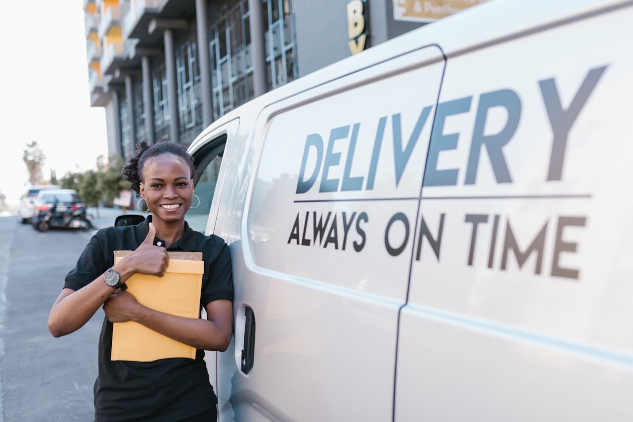hero-img-02 A cheerful delivery woman standing by a van with a parcel, ready for delivery.